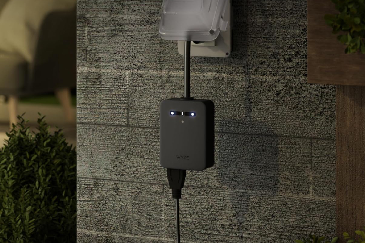 A black Wyze outdoor plug against a stone wall.