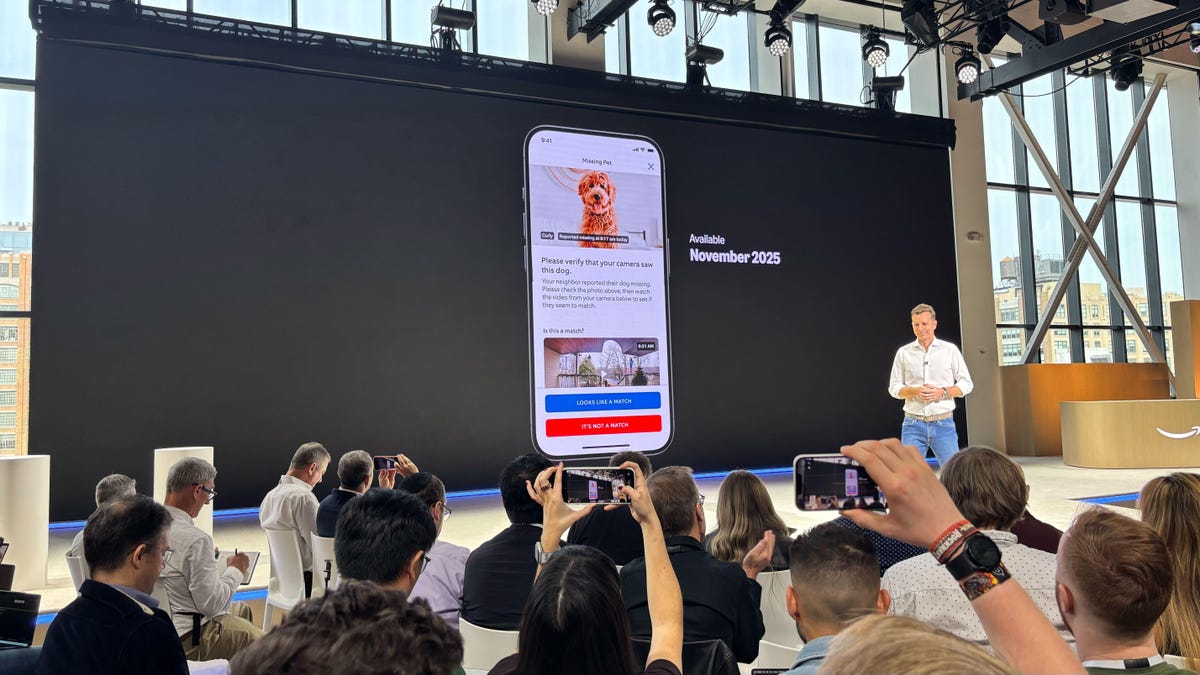 An executive for Amazon-owned Ring stands on a stage at a press event announcing the company's Search Party feature for finding lost dogs. On a screen behind the presenter, a screenshot of one of Ring's apps is shown with an image of a dog.