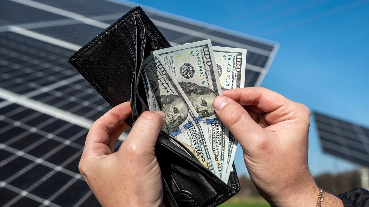 A person opening a wallet full of cash in front of solar panels