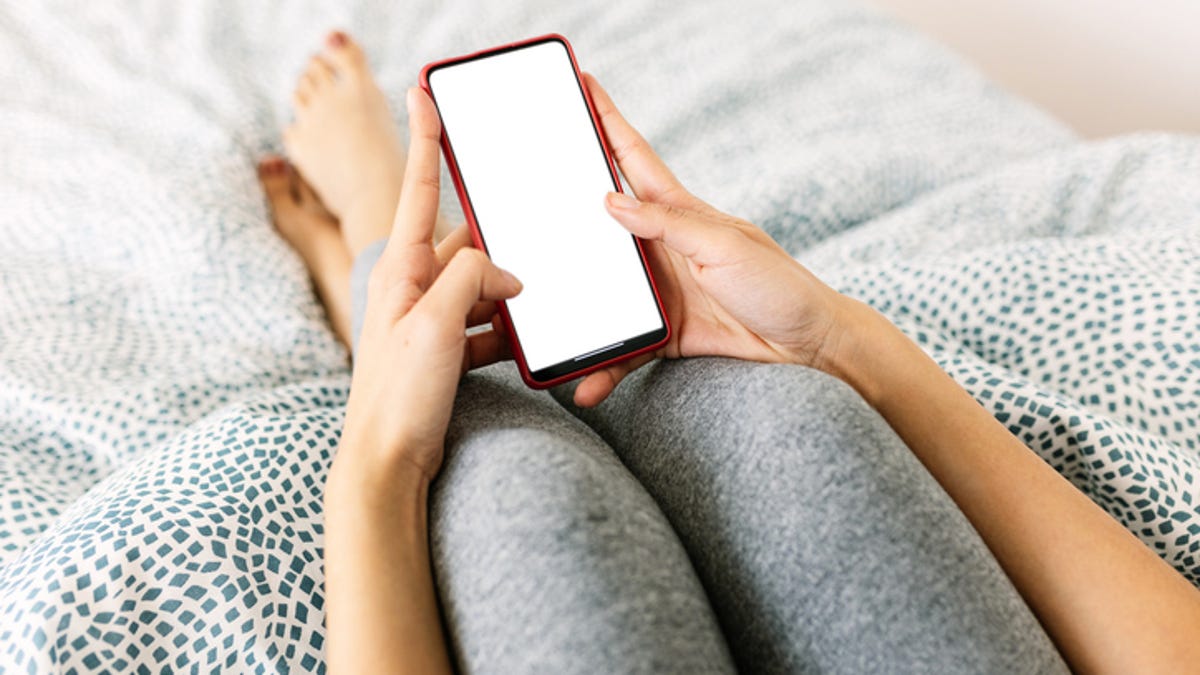 Woman's knees sitting on bed holding smartphone in both hands