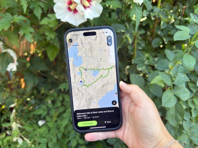 A hand holds a phone with the AllTrails app displaying a map