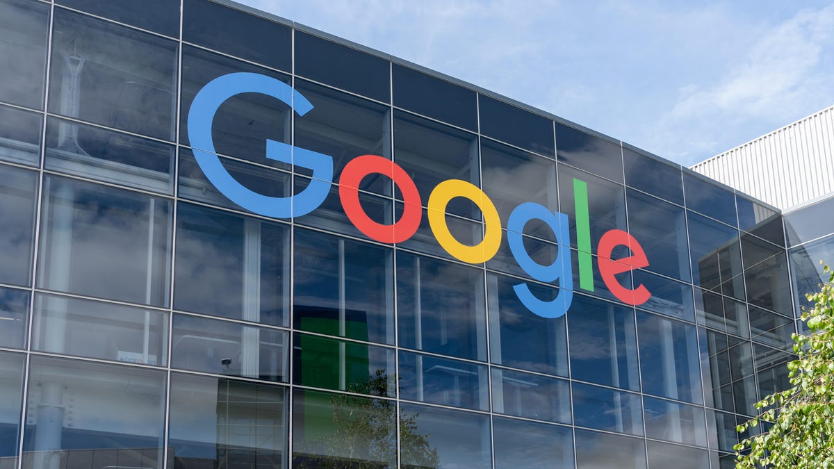 the exterior of Google headquarters in Mountain View, California. the rainbow letters of GOOGLE are positioned on the front of a glass facade