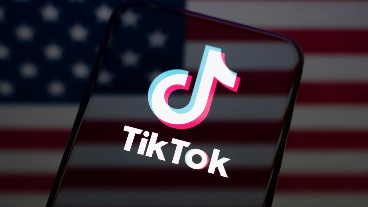 a phone with the TikTok logo is shown in front of a blurred US flag