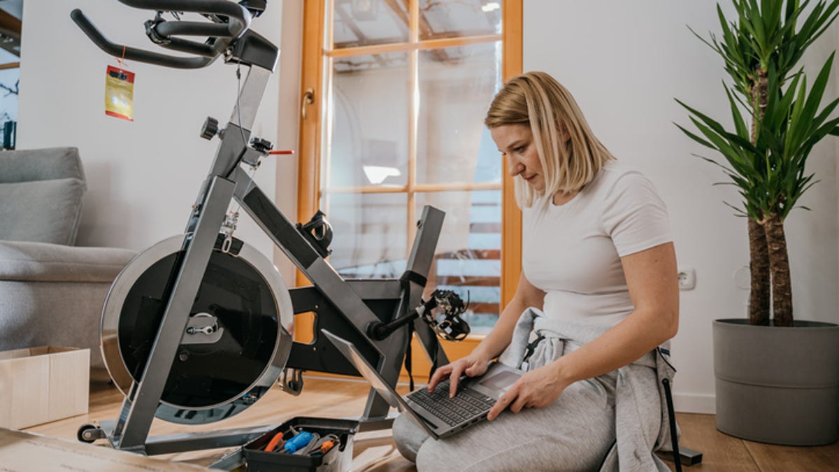 Woman sitting next to exercise bike with a laptop and toolbox