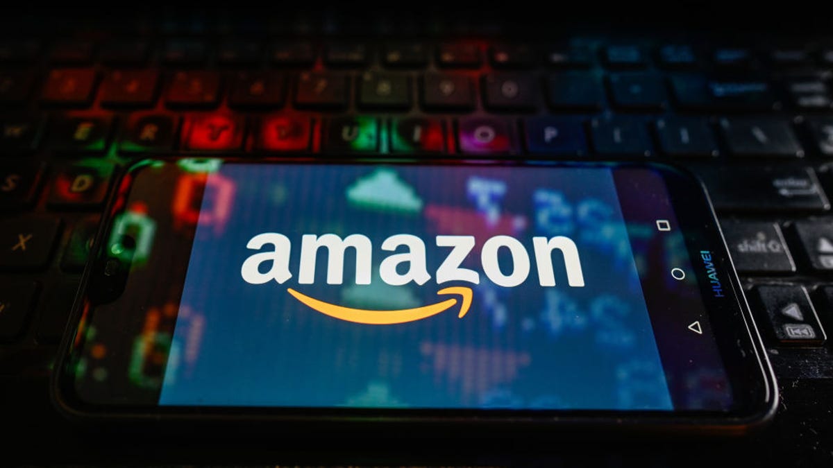 A dark photo of a keyboard with a phone displaying the Amazon logo on top