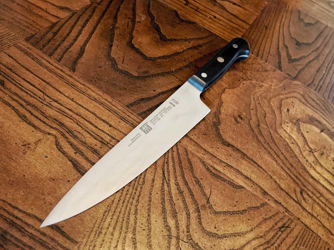 Zwilling Gourmet 8-inch Chef's Knife on a brown wooden table.