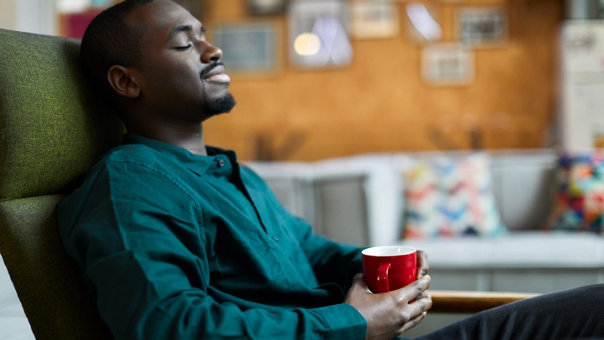 Man relaxing with his eyes closed in a chair, enjoying a cup of coffee
