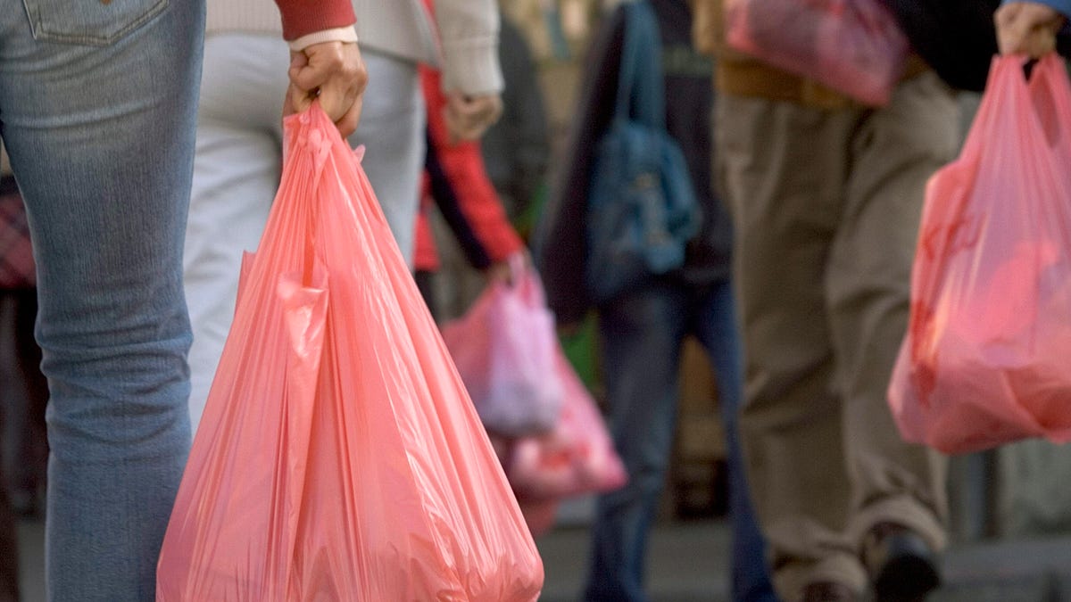 A group of people on the street carrying red plastic grocery bags.