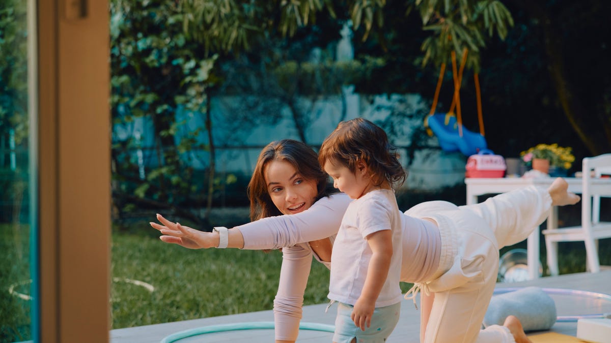 A person performing yoga in a backyard next to a child.