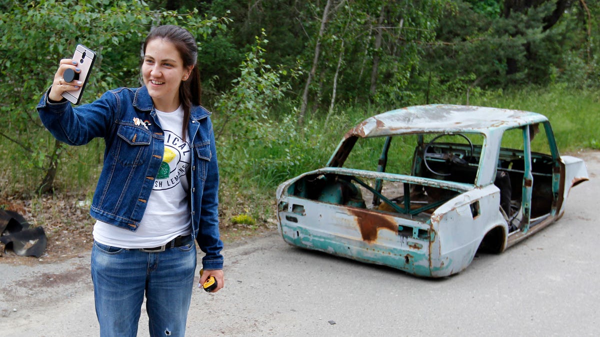A visitor posses for a selfie next a wrecked car at the