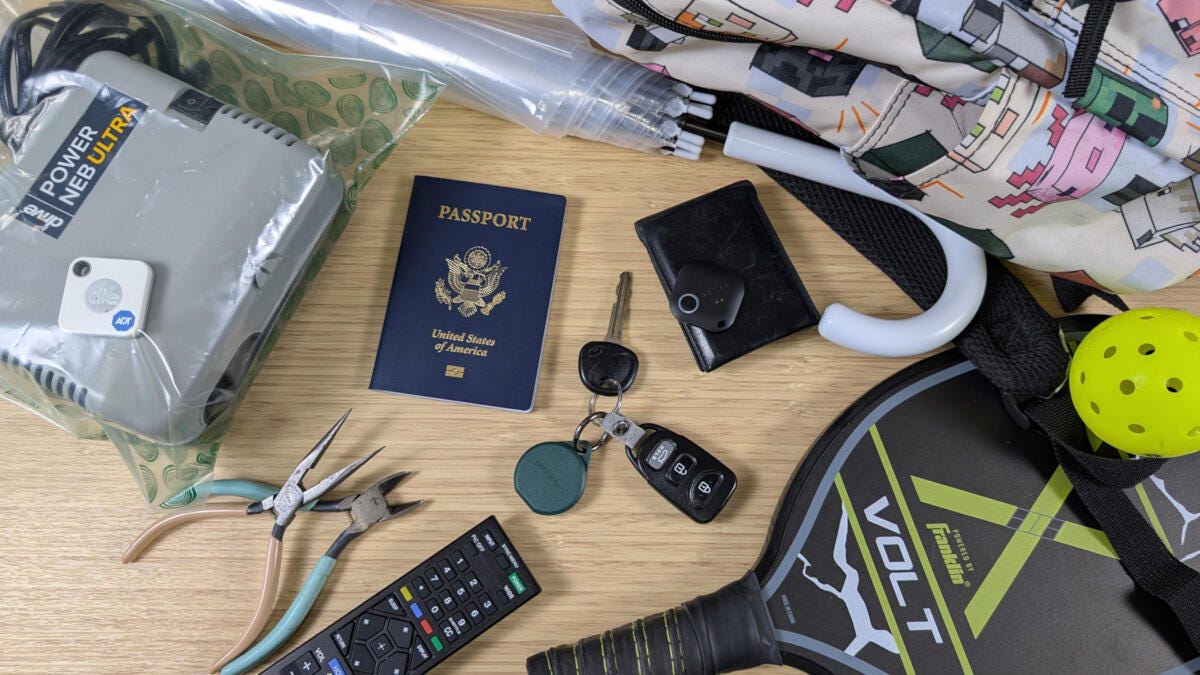 bluetooth trackers and various trackable items on bamboo desk including a passport, car keys and umbrella