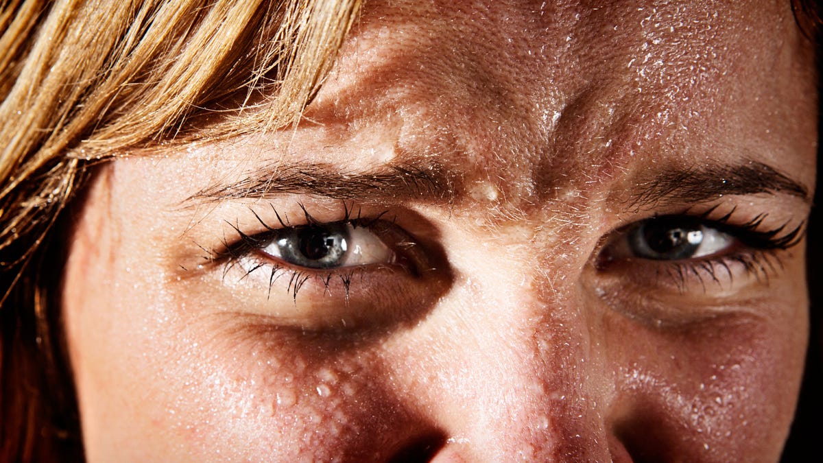 Close zoom-in of woman's scrunched eyes with beads of sweat