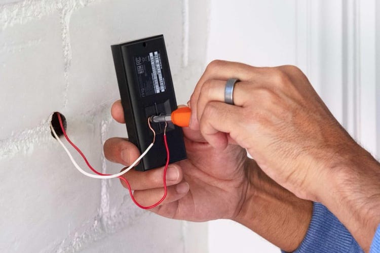 Hands screw in wires for the Ring video doorbell against white stucco.