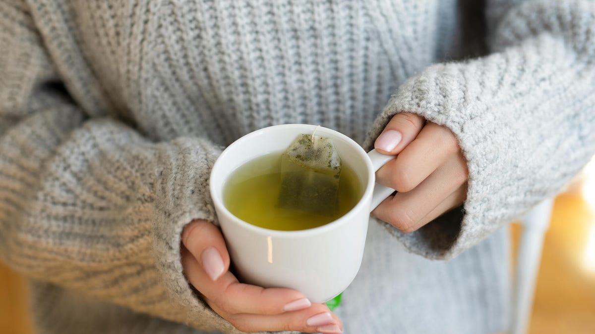 Woman in grey sweater holds a cup of hot green tea