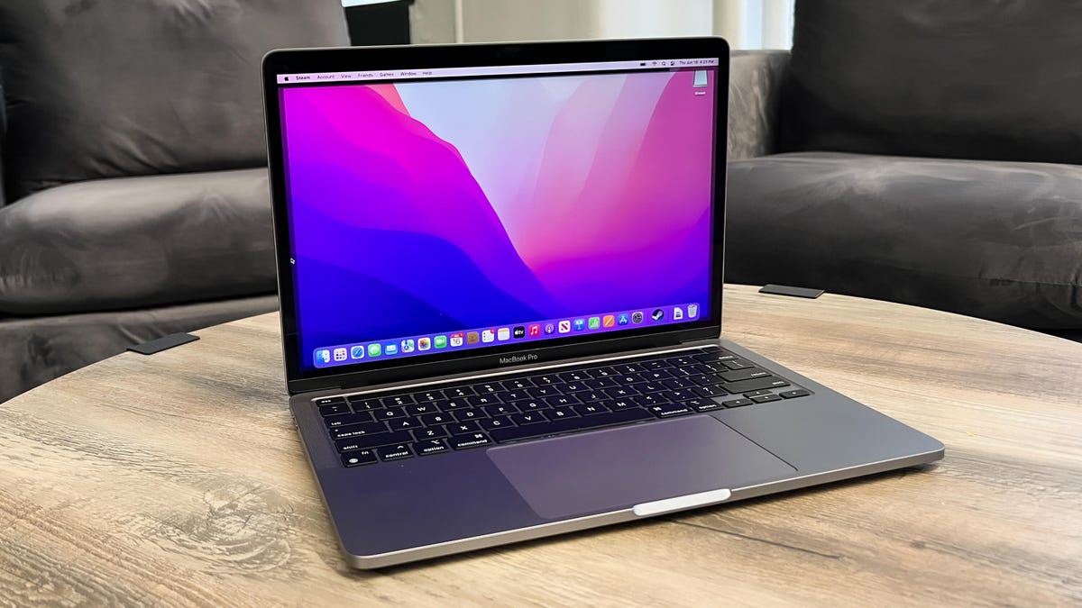 An Apple MacBook Pro open on a table with sofa chairs behind it
