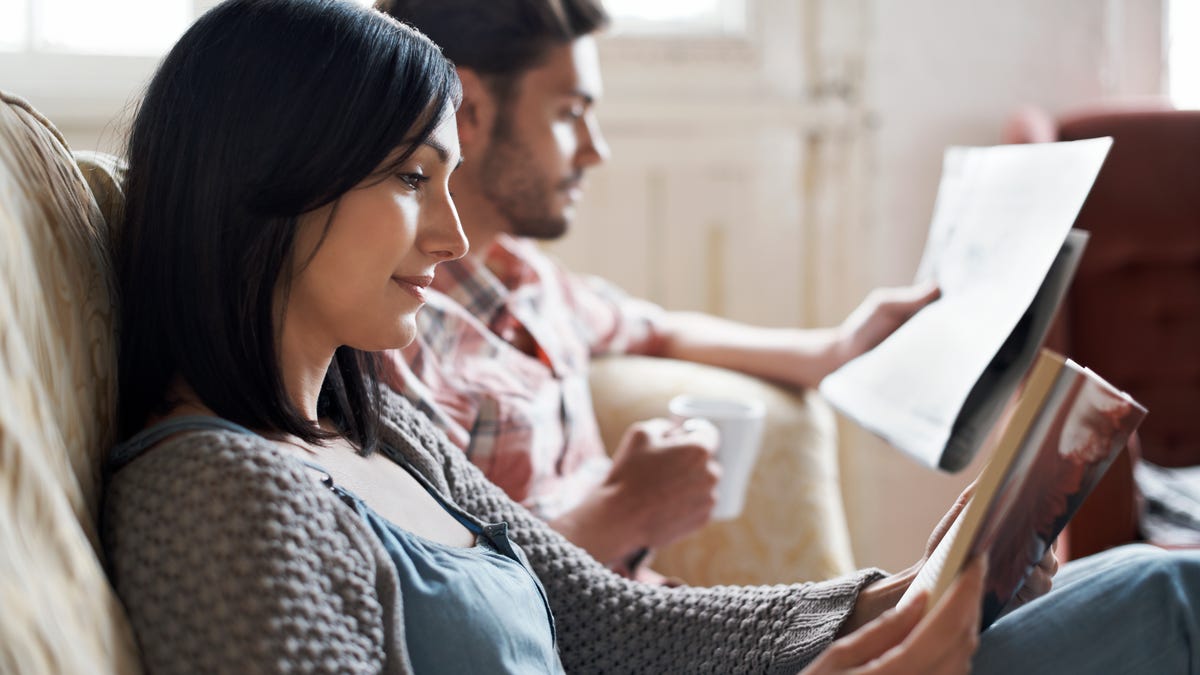 A couple sits next to each other on the couch, both reading.
