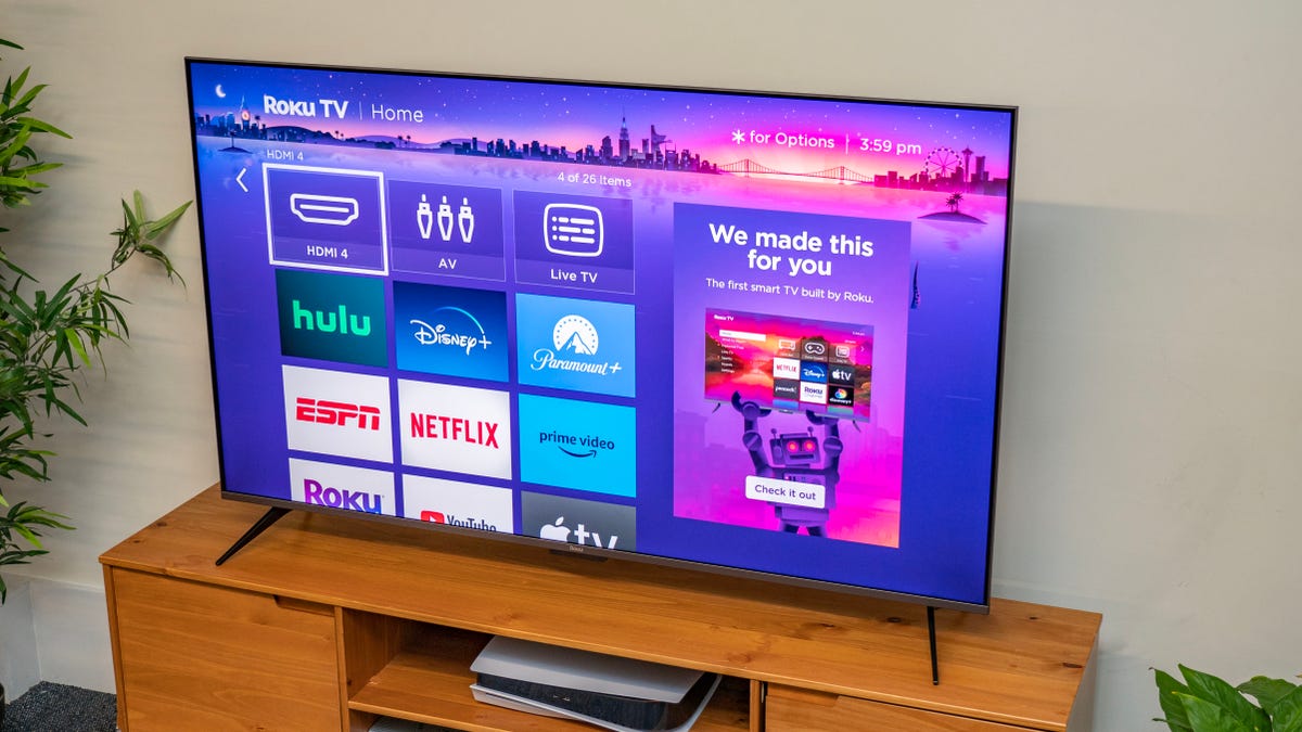 The Roku interface displayed on a flat-screen TV, sitting on a wood entertainment cabinet