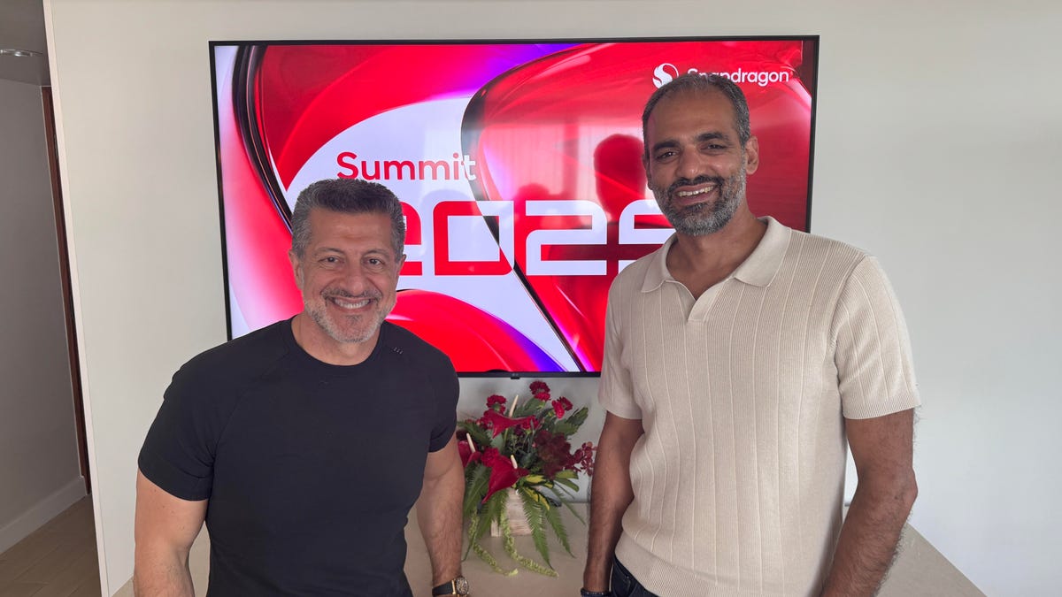 Two men smile and stand in front of a TV with the Snapdragon Summit 2025 logo.