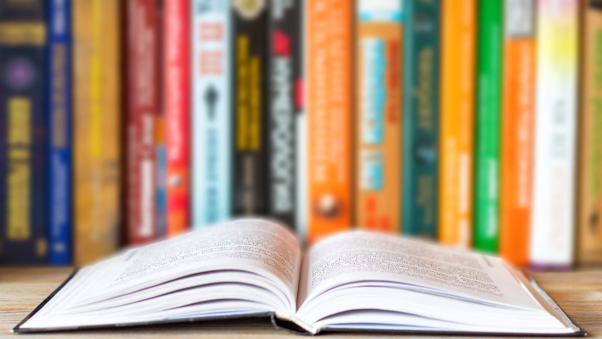 Image of book open flat in front of a shelf of books.