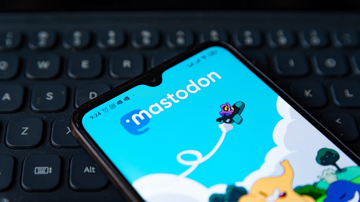 A phone with the Mastodon home page on its screen that is held above a computer keyboard