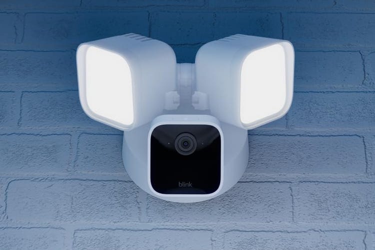 A Blink floodlight camera on a white brick wall.