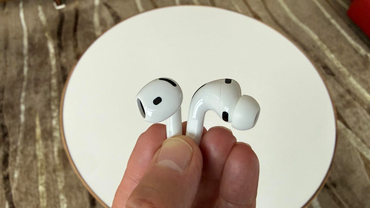 two single white earbuds from apple that are held up in comparison by author's hand