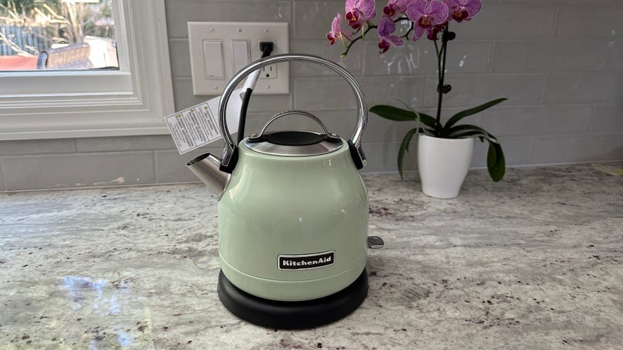 A pistachio green-colored KitchenAid KEK1222 electric kettle sits on a granite countertop.