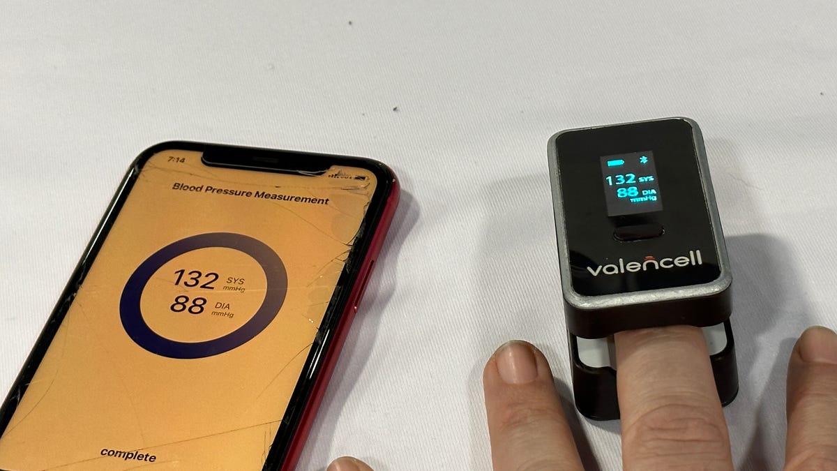 A finger-attached blood pressure monitor next to a phone