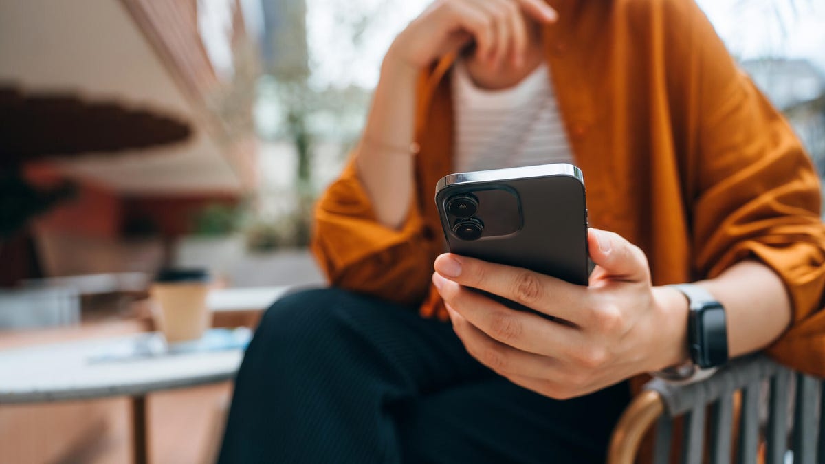 A person holds their cell phone while sitting at a cafe.