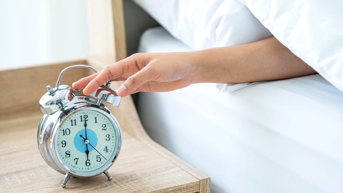 Closeup of hand stopping alarm clock from ringing.
