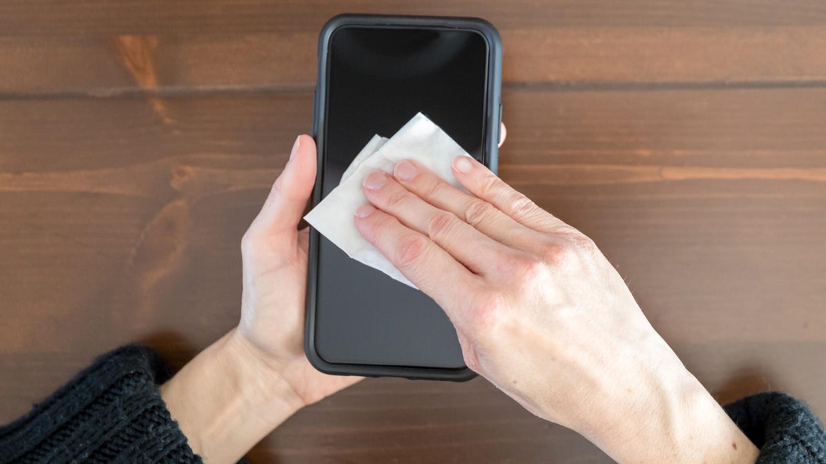 Woman cleaning display of smart phone with antibacterial white tissue.