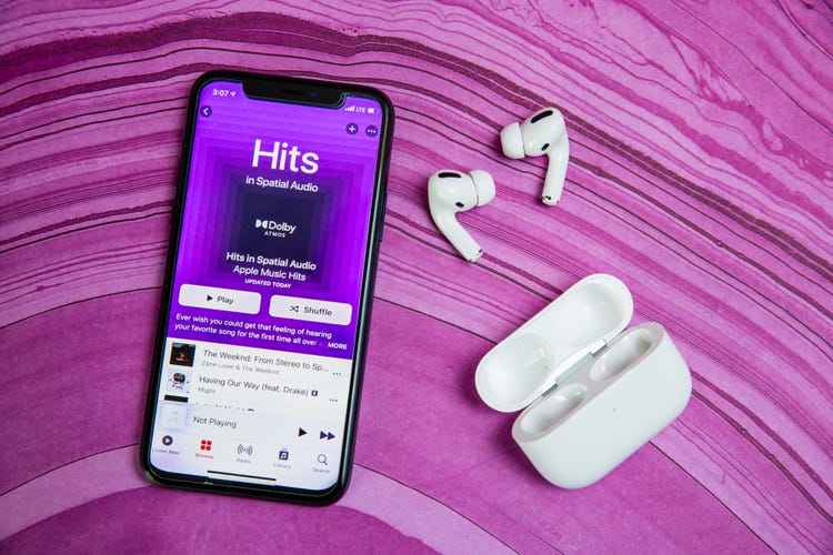 A pair of AirPods Pro lies next to a cell phone playing music from  Apple Music