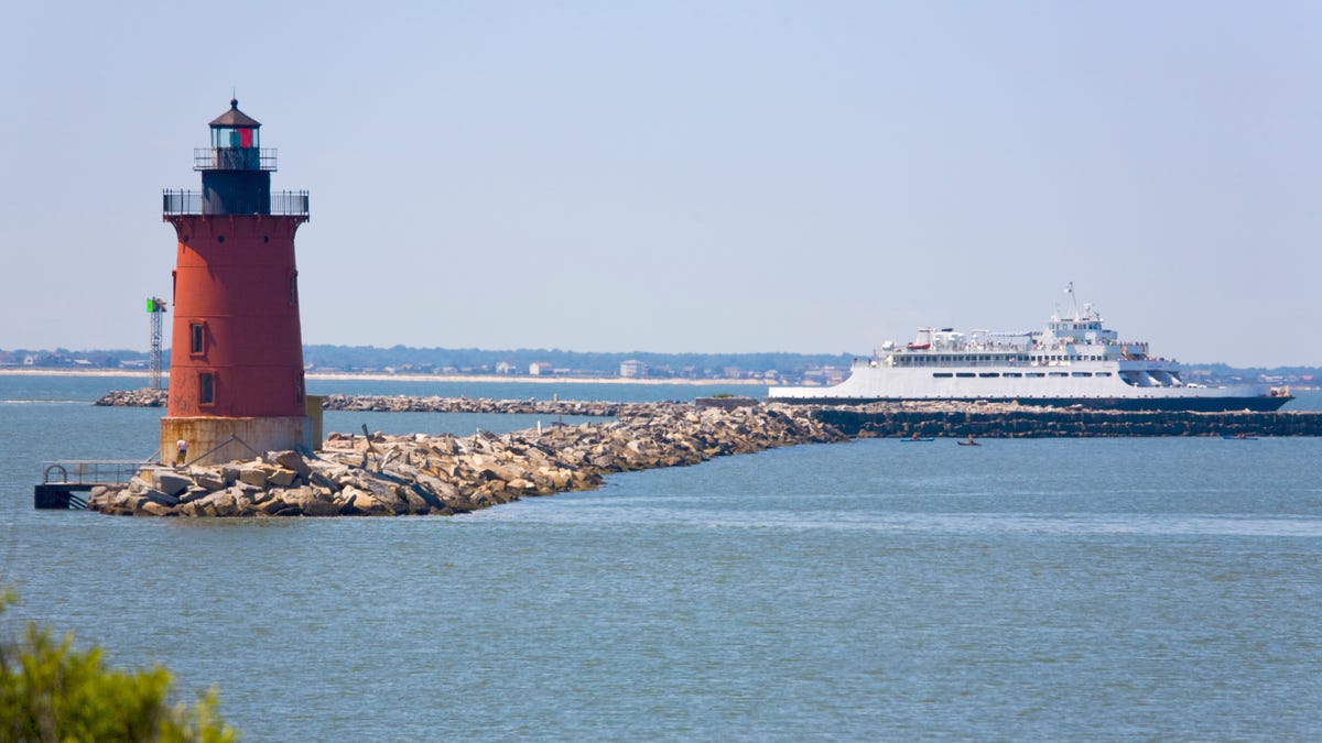 lighthouse on the water with a large boat in background.