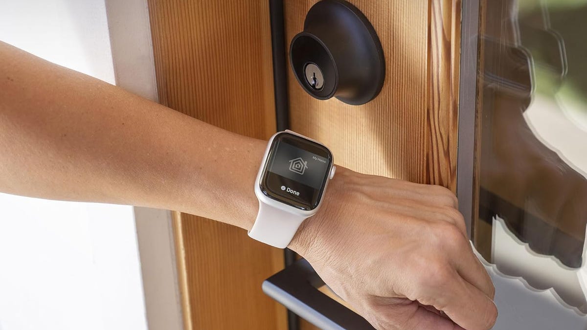 A hand with an Apple Watch activates a Level Lock Plus on a wood door.