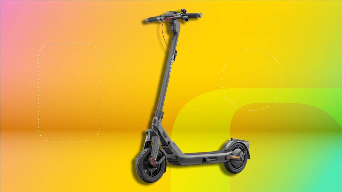 Modern black electric scooter with red wheel accents, digital display, and sleek frame—designed for urban commuting. Positioned against a vibrant gradient background transitioning from pink and orange to yellow and green.