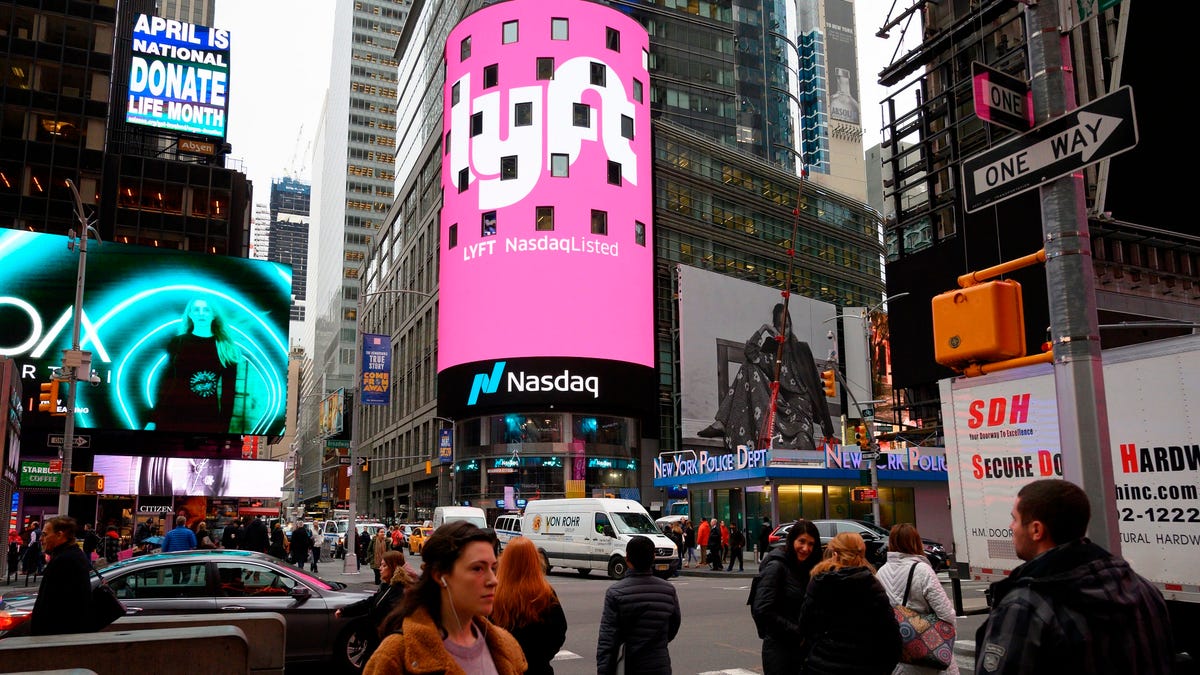 A busy midtown New York City street near Times Square is awash in noise and color, including bright pink emanating from a Lyft video billboard above the Nasdaq offices.