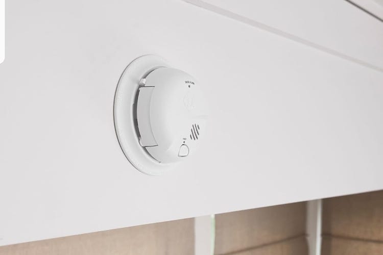 A white First Alert battery detector on white shelving.