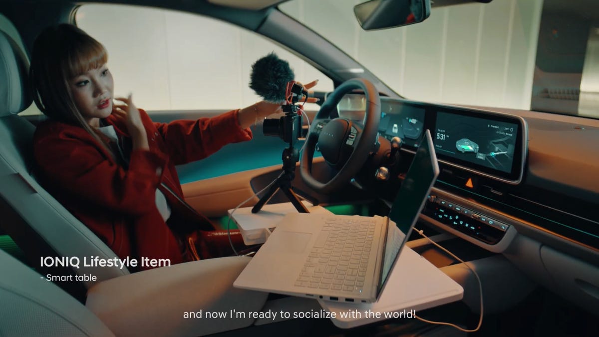 Woman in driver's seat using a camera and laptop with the deployable Ioniq 6 Smart Table