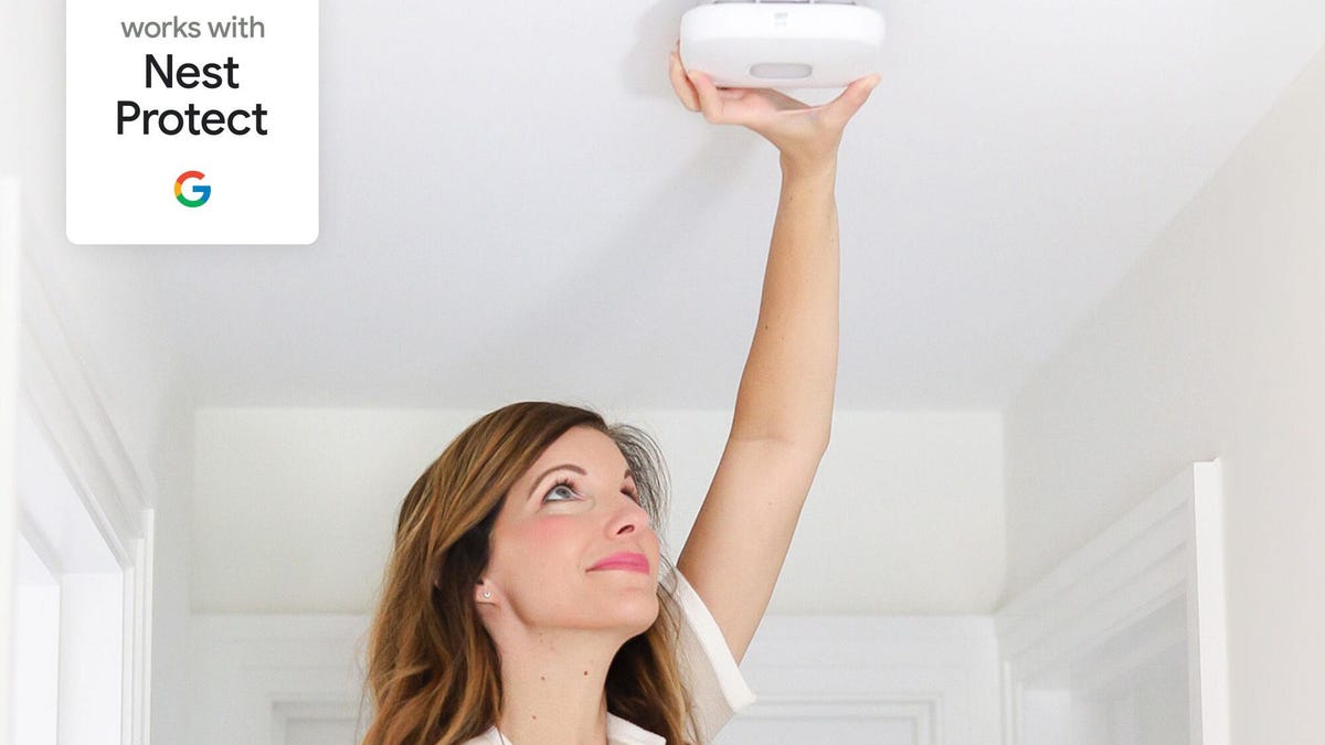 Woman installing Google Home compatible First Alert detector on white ceiling.