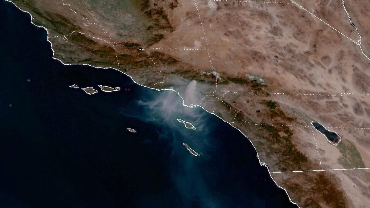 Full color satellite view of Los Angeles area shows large gray smoke plumes from multiple wildfires.