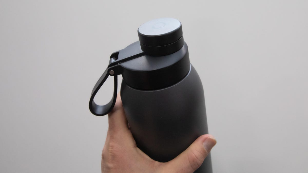 A black stainless steel water bottle is held in a hand