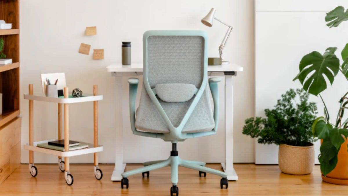 mint green rolling office chair in front of white desk, gray lamp, rolling caddy to the left in a white office with wooden floor