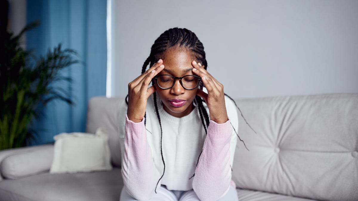 A young woman is sitting on the sofa at home with her head in her hands experiencing stress