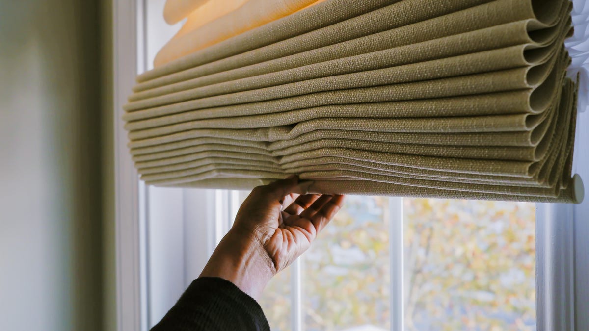 A person adjusts fabric blinds in front of a window.
