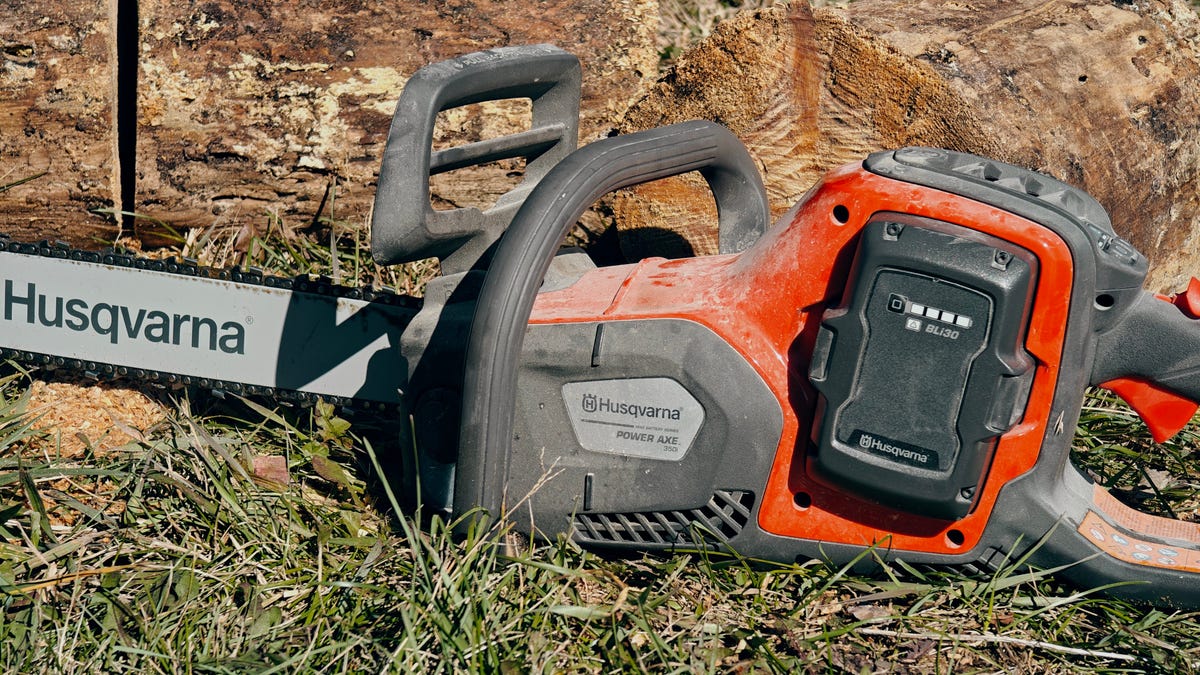 Husqvarna Power Axe 350i chainsaw sitting on the ground by some logs