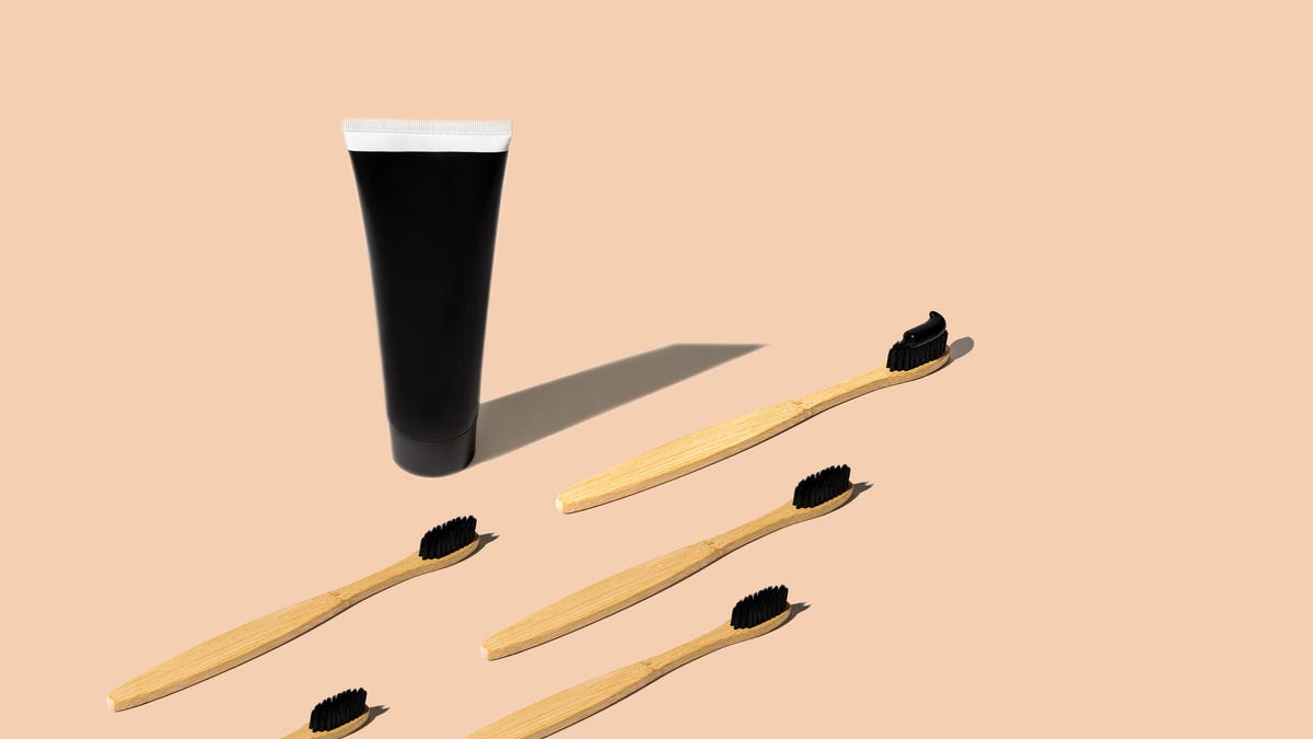 A tube of charcoal toothpaste next to five toothbrushes against a peach background