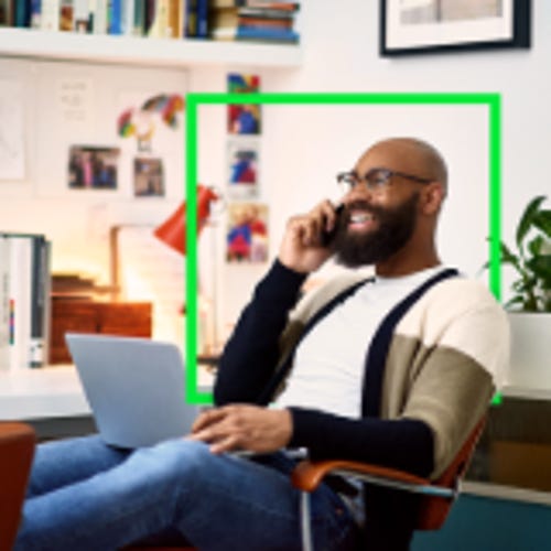 man sitting at a desk with laptop in lap and talking on a cellphone