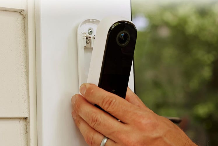 A hand places the Arlo 2K doorbell on its base, attached to white external house trim.