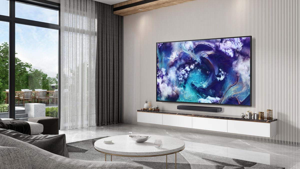 product shot of a big TV mounted on the wall of a room with high ceiling and large windows