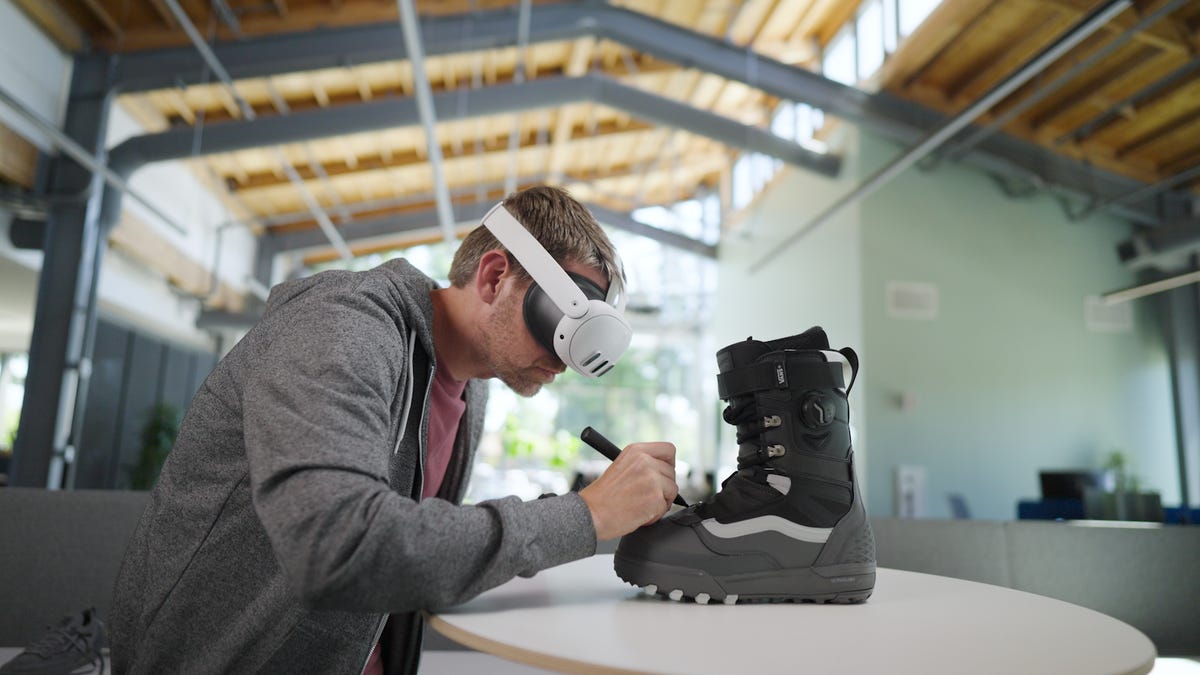 Someone wearing a Quest 3 headset and using a stylus to draw on a shoe in VR